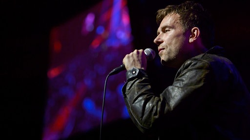 Portrait Damon Albarn auf der Bühne mit Mikrofon