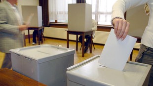 Eine Wählerin steckt bei den Kommunalwahlen ihre Stimmzettel in die Wahlurne