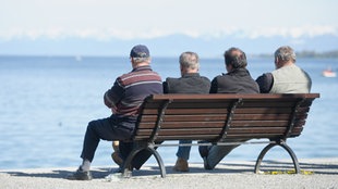 Vier Herren fortgeschrittenen Alters sitzen in Konstanz auf einer Bank am Ufer und blicken auf den Bodensee hinaus