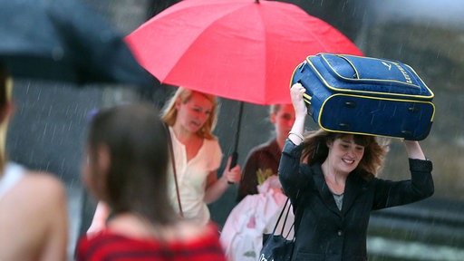 Junge Frau schutzt sich im Regen mit ihrem kleinen Lufthansa-Koffer