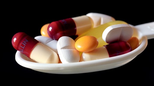 Medicinska kašika puna različitih tableta i kapsula na crnoj pozadini