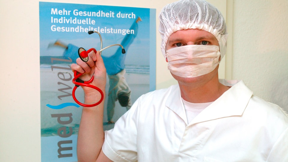 Arzt mit Stethoskop steht vor einem Plakat, auf dem für die IGeL Leistungen geworben wird