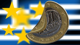 Savijeni novčić od jedan evro a u pozadini zastava Grčke