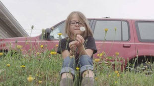 Screenshot aus dem Kurzfilm Tomgirl: Jake auf einer Wiese mit Löwenzahn in der Hand