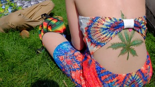 Junge Frau mit Marihuana-Tattoo sitzt in einem Park in Denver