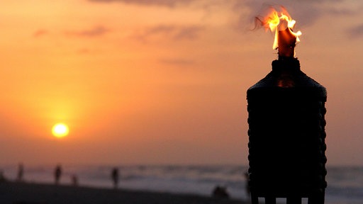 Eine brennende Fackel im Sonnenuntergang am Strand von Palomino