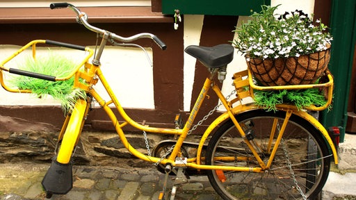 Postfahrrad mit Blumen im Gepäckkorb vor einem Fachwerkhaus